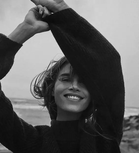 Femme souriante en pull noir au bord de la mer